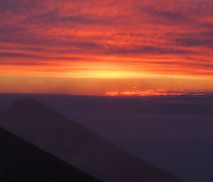 An orange and purple sunset behind two mountain peaks