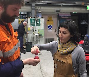 A woman holding a red egg is showing a man holding a red egg how to crack them together