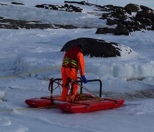 a man in an orange freezer suit stands on ice holding a rescue platform