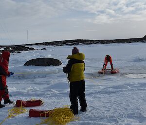 a man on a rescue platform is being dragged ashore by two expeditioners holding ropes