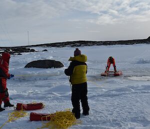 a man on a rescue platform is being dragged ashore by two expeditioners holding ropes