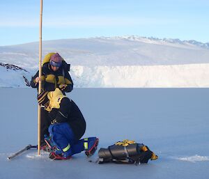 two people place a cane stick in the ice with a glacier edge in the background