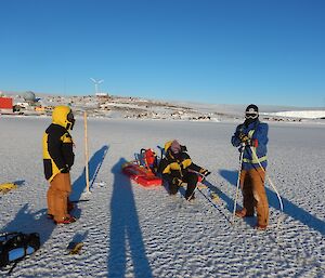 three people mark a sea ice drilling spot with a cane