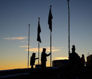 two men hold flag poles with a sunrise in the background