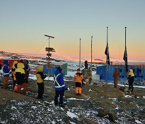 a group of expeditioners stand in front of Australian and New Zealand flags at half mast