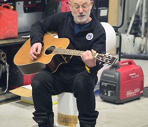 a man sitting on a tub plays the guitar