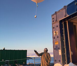 A man releases a large white balloon into the sky