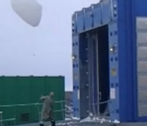 A man appears to grapple with a large white weather balloon before releasing it