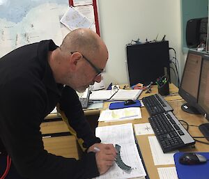 A man writes on a piece of cardboard at a desk