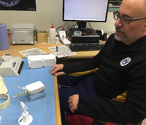 A man sits at a desk with a white plastic radio sonde in front of him