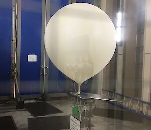 A white balloon is being filled with hydrogen by a machine