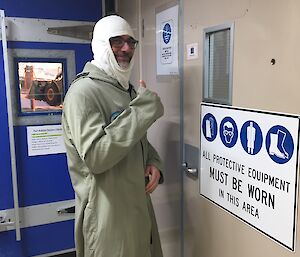 A man stands covered from head to toe in front of a door with thumbs up