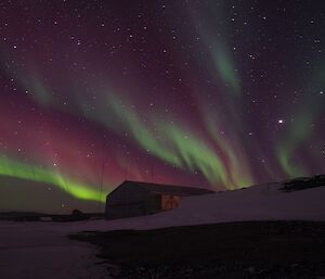 A violet coloured aurora rises above an old metal hangar