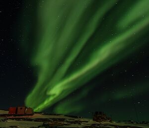 A green streak in the black sky behind three red buildings that used to be kennels for husky dogs