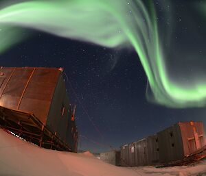 Two old buildings are lit up by a green and white aurora