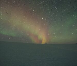 A rainbow of pink rises above an icy plateau