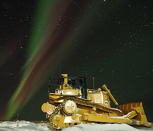 A yellow bulldozer with a backdrop of purple and green