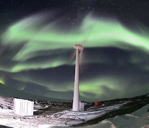 A wind turbine is in the middle of a circular green and white aurora