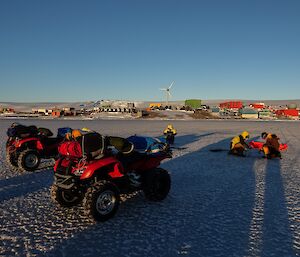 Two quad bikes re parked on ice, three people are crouched on the ice