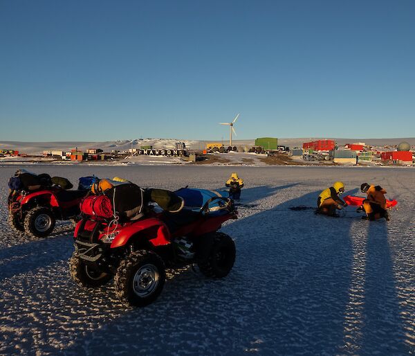 Two quad bikes re parked on ice, three people are crouched on the ice