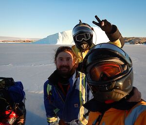 Three men stand in front of an iceberg