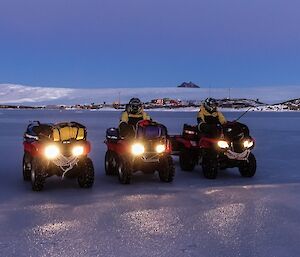 Four quad bikes are parked on ice with the station in the background