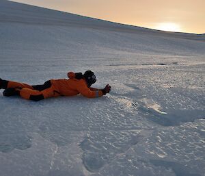 A man in a yellow freezer suit lays outstretched on the ice