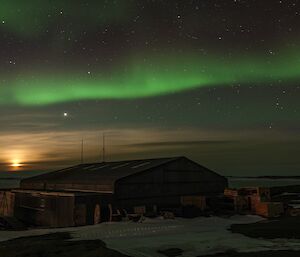 A green aurora and the moon over a silver hangar