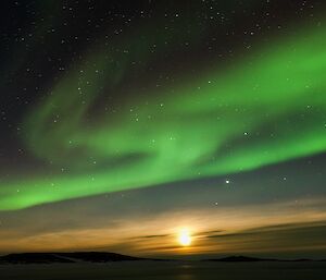 A green swirl of an aurora above a yellow moon