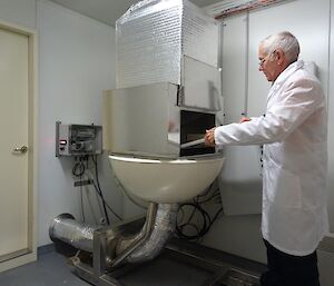 A man in a white coat stands in front of a air sampling machine