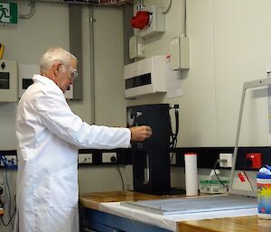A man in a white coat stands in front of a pressing machine