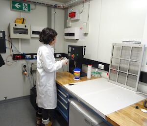 A woman in a white coat stands in front of a machine press
