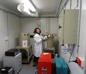 A woman in a white coat stands in front of a round detector machine