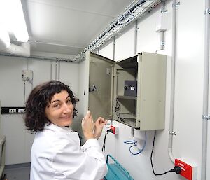 A woman in a white coat stands in front of a metal cabinet