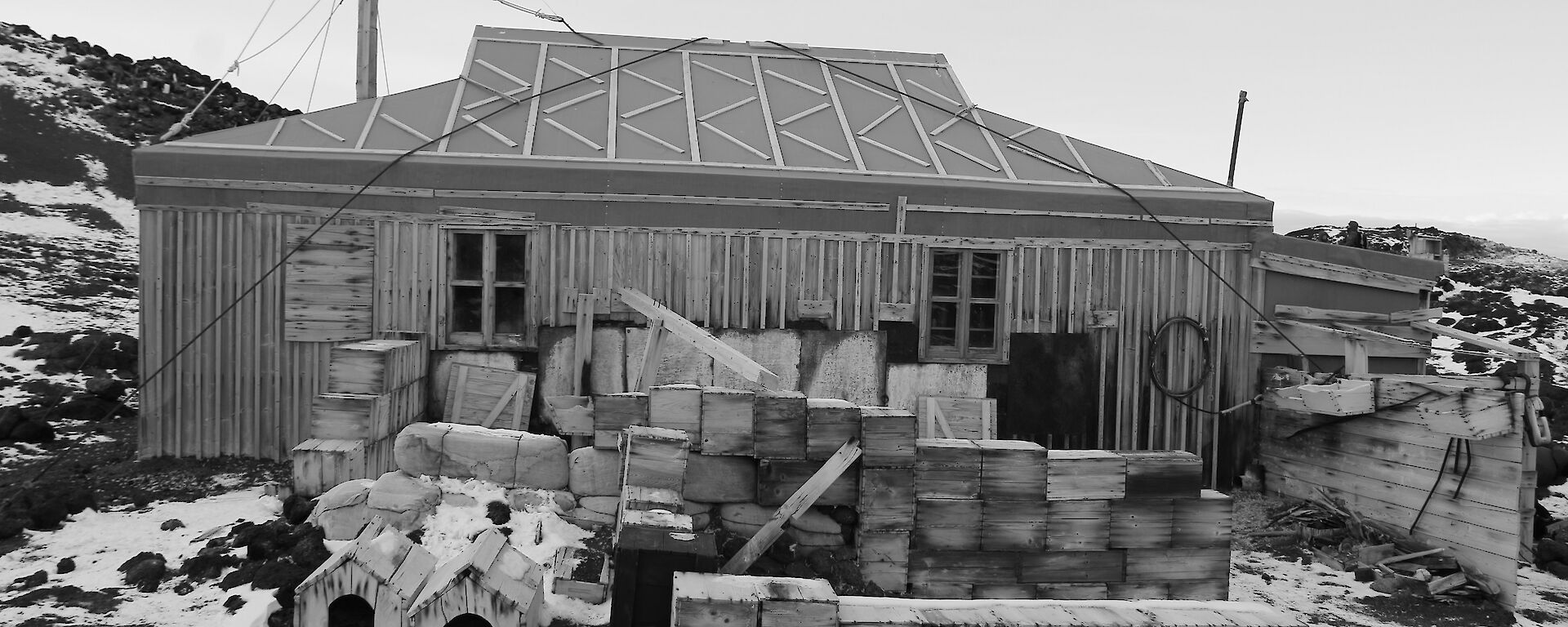 A black and white photo of a wooden hut in snow