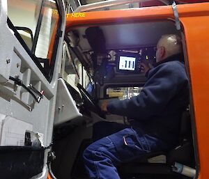 A man sits in an orange Hägglunds vehicle inspecting a screen