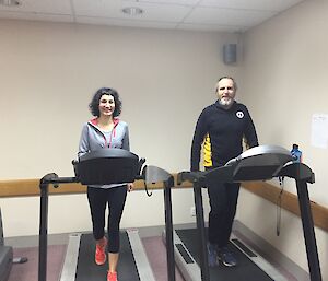 A woman and a man walk side by side on treadmills