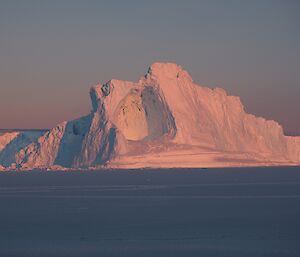 An iceberg is illuminated in pink light