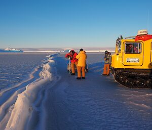 Three men drill the sea ice next to a yellow Hägglunds, with a long pressure ridge of ice beside them