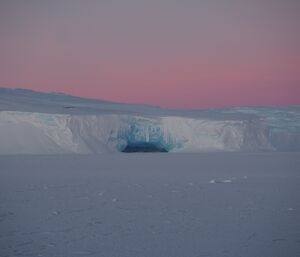 A pink sky over a blue ice cave