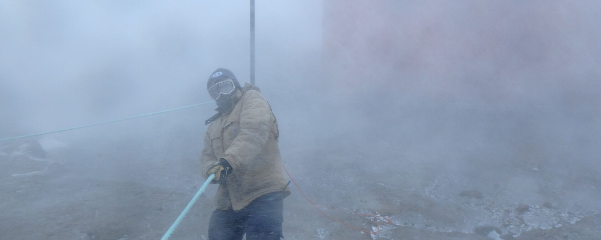 A man is holding on to a blizzard line in blowing white snow