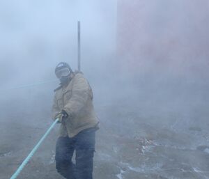 A man is holding on to a blizzard line in blowing white snow