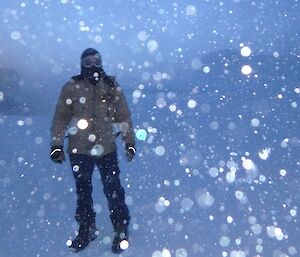 A man stands in a white blizzard surrounded by snow flakes