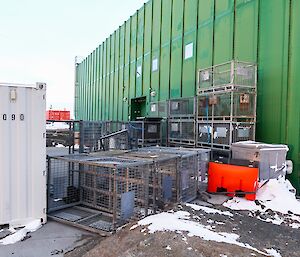 A series of containers and storage cages are bunched up together next to a green building