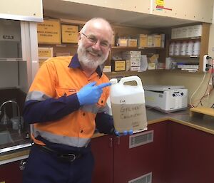 A man in high visibility clothing stands in a laboratory holding a container of liquid