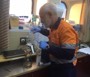 A man in high visibility clothing stands in front of filtration equipment in a laboratory