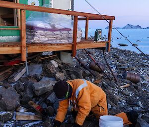 A man in a yellow freezer suit is kneeling on rock collecting debris