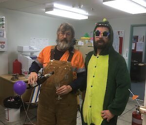 One man holds a bottle of champagne the other man wears a dinosaur costume