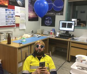 A man in a yellow shirt has a balloon tied to his glasses