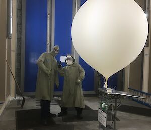 two men in protective clothing stand next to a hydrogen filled balloon